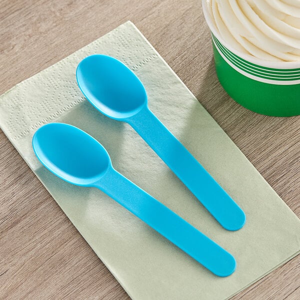 Two blue Choice heavy weight plastic spoons on a napkin next to a cup of ice cream.