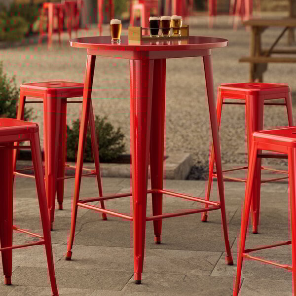 A Lancaster Table & Seating Ruby Red Bar Height Outdoor Table with red bar stools on an outdoor patio.