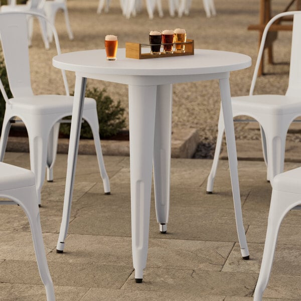 A Lancaster Table & Seating white metal outdoor table on a stone surface with white chairs.