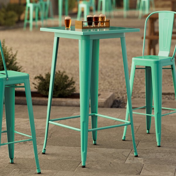 A Lancaster Table & Seating aquamarine table with a pole in the middle and green chairs.