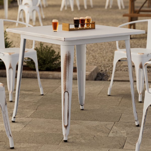 A Lancaster Table & Seating distressed pearl white table with drinks on it.