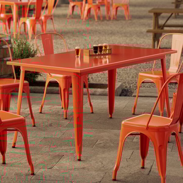 A Lancaster Table & Seating Alloy Series standard height outdoor table in amber orange on a stone patio with orange chairs.