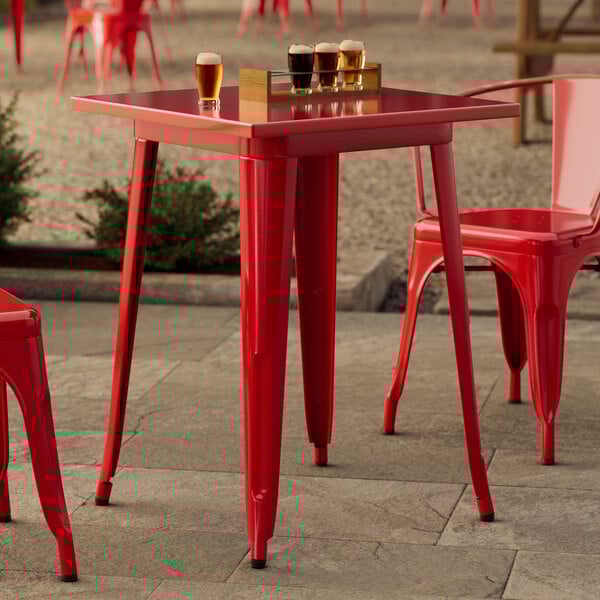 A Lancaster Table & Seating ruby red table with red legs on an outdoor patio.