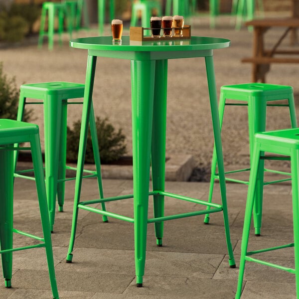 A Lancaster Table & Seating jade green bar height table with green stools on a concrete patio.