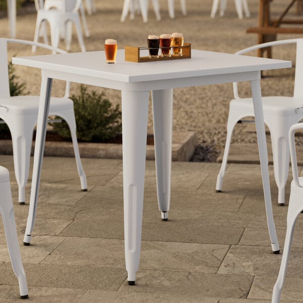 A Lancaster Table & Seating white table on an outdoor patio with glasses of beer on it.