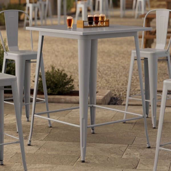 A Lancaster Table & Seating bar height outdoor table with drinks on it and metal chairs on a patio.