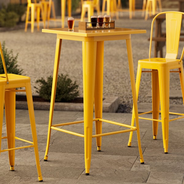 A Lancaster Table & Seating citrine yellow bar height table with a yellow metal bar.