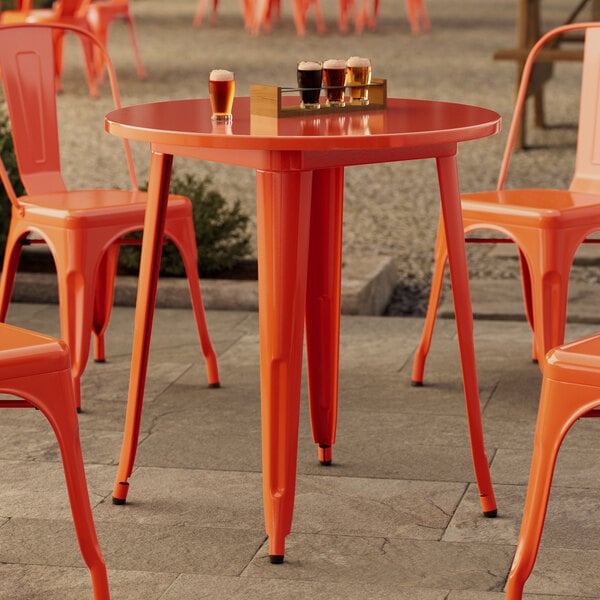 A Lancaster Table & Seating outdoor table and chairs set up on a stone patio with orange chairs.