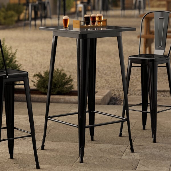 A Lancaster Table & Seating black metal bar height table on an outdoor patio.