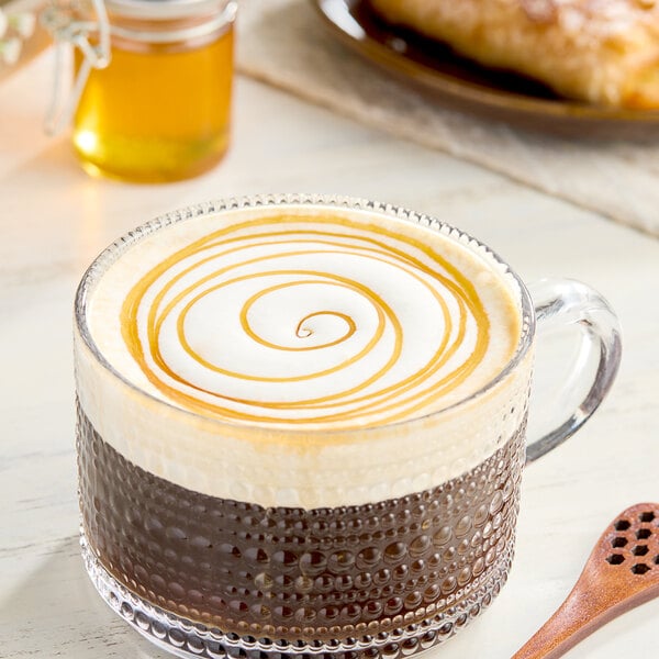 A glass of coffee with a swirly caramel top next to a jar of Hometown Provisions Wildflower Honey.