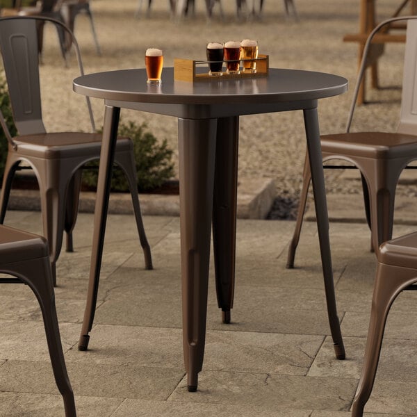 A Lancaster Table & Seating round copper outdoor table with a drink on it.