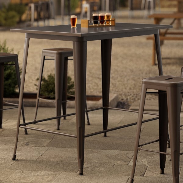 A Lancaster Table & Seating rectangular copper bar height table with a group of glasses of beer on it outdoors.