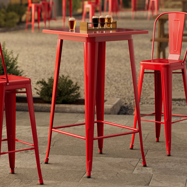 A Lancaster Table & Seating ruby red metal bar table with chairs on an outdoor patio.