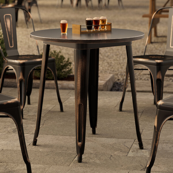 A Lancaster Table & Seating round distressed copper table and chairs on a stone patio.