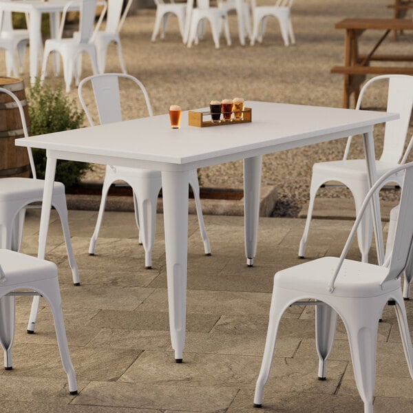 A Lancaster Table & Seating pearl white table on a patio with white chairs.