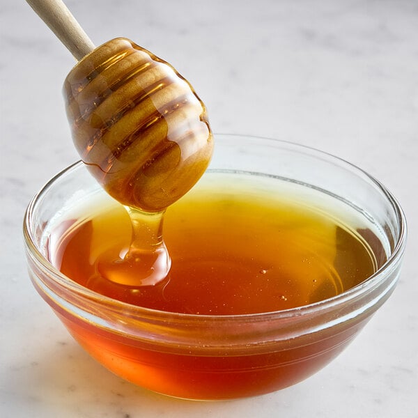 A honey dipper dripping honey into a glass bowl.
