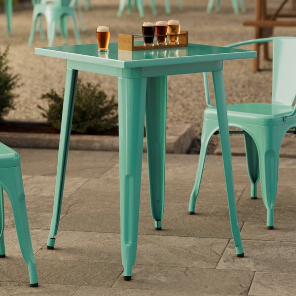 A Lancaster Table & Seating aquamarine table on a concrete patio with chairs and drinks.