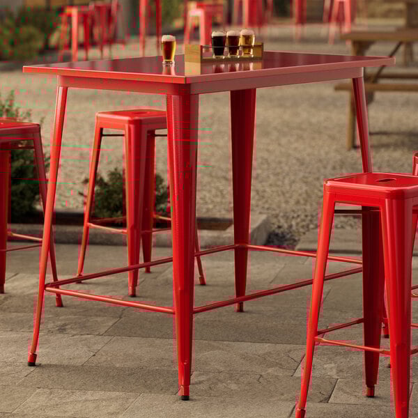 A red metal bar table with red stools on an outdoor patio.