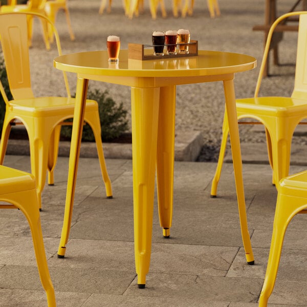 A Lancaster Table & Seating citrine yellow metal table and chairs set up on an outdoor patio.