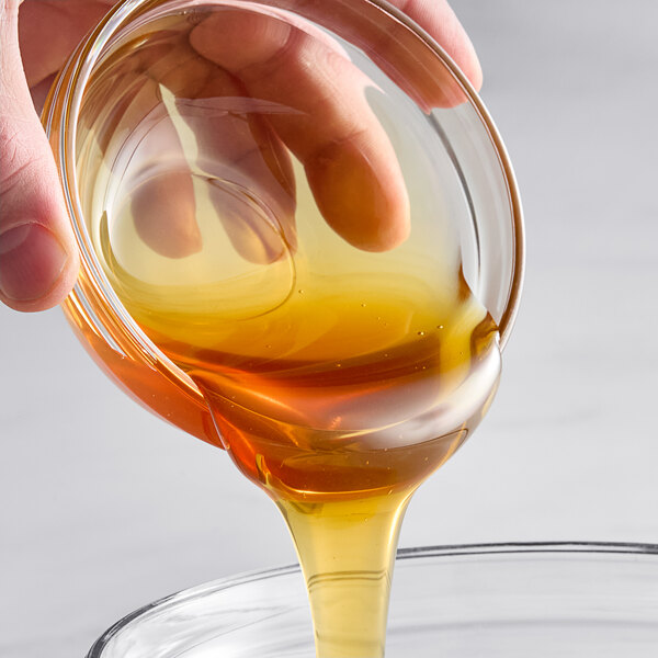 A hand pouring Hometown Provisions Alfalfa Honey into a glass bowl.