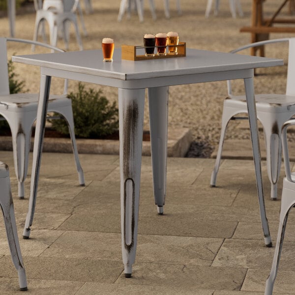 A Lancaster Table & Seating distressed nickel gray outdoor table on a patio with glasses of beer on it.