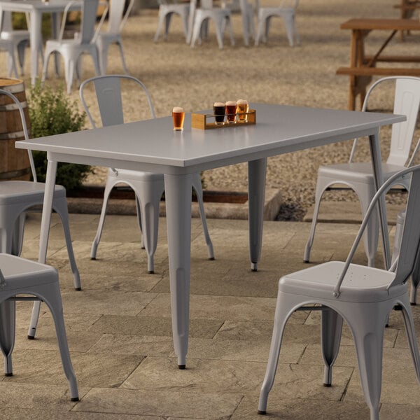 A Lancaster Table & Seating Alloy Series nickel gray table with legs and chairs on an outdoor patio.
