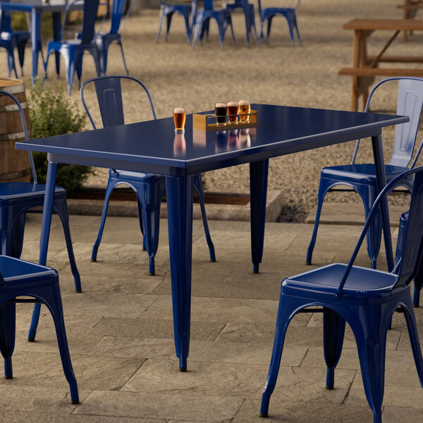 A Lancaster Table & Seating sapphire blue metal table with blue chairs on an outdoor patio.