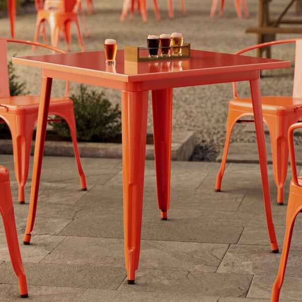 A Lancaster Table & Seating orange metal table with chairs on an outdoor patio.