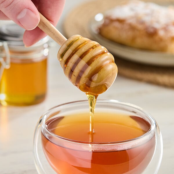 A hand holding a wooden honey dipper over a cup of tea.