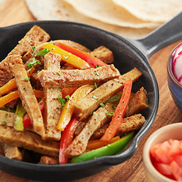 A pan of seitan next to a tortilla and a bowl of salsa.