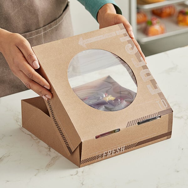 A person holding an Innopak Kraft bakery box with a clear window containing a pie.