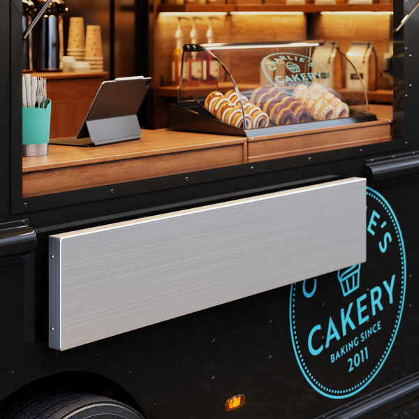 A Regency aluminum folding concession shelf holding trays of pastries in a food truck.