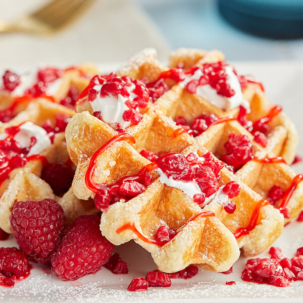 A plate of waffles with raspberries, cream, and syrup.