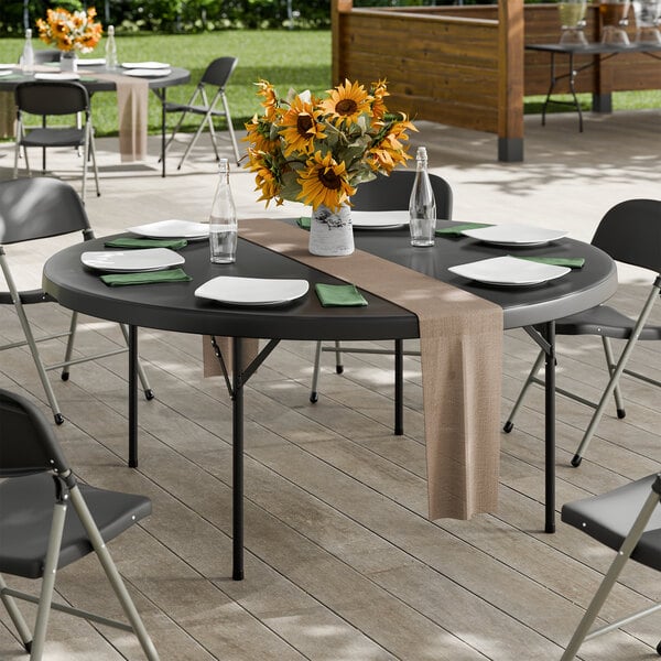 A 72-inch round black heavy-duty blow molded plastic folding table with black legs, set for dining outdoors.