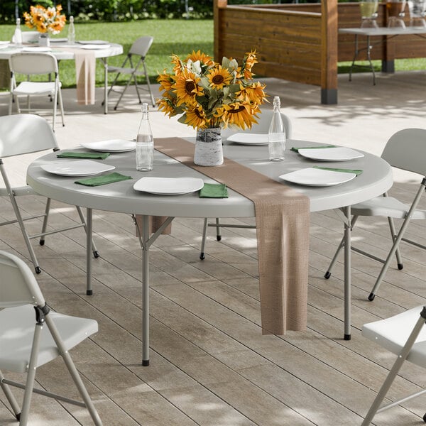 A large round gray folding table with gray legs, set for dining and decorated with a vase of sunflowers.