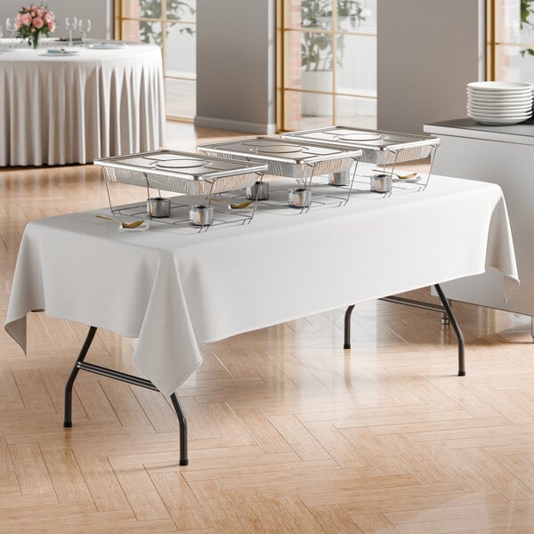 A rectangular black folding table with black legs, set up for catering with chafing dishes and a white tablecloth.