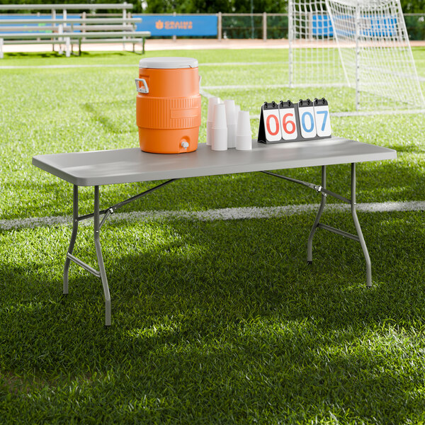 A gray heavy-duty blow molded plastic folding table with gray legs set up on a sports field.