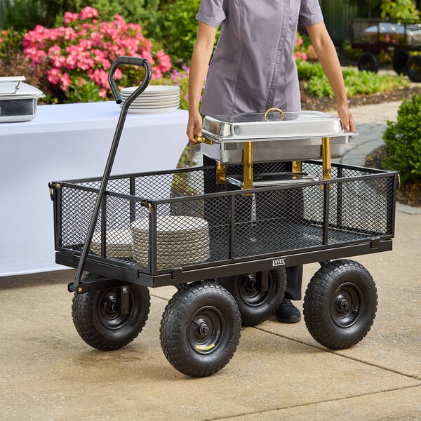 A woman using a Lavex steel garden/utility cart to carry plates in an outdoor setup.