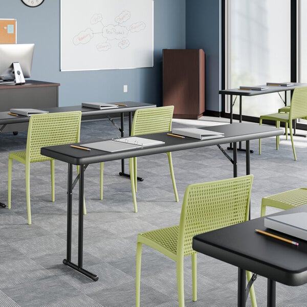 An 18 by 72 inch black heavy-duty blow molded plastic folding table with black legs, set up in a classroom setting.