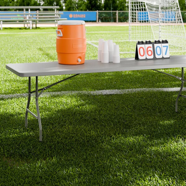 A gray heavy-duty blow molded plastic folding table with gray legs set up on a sports field.