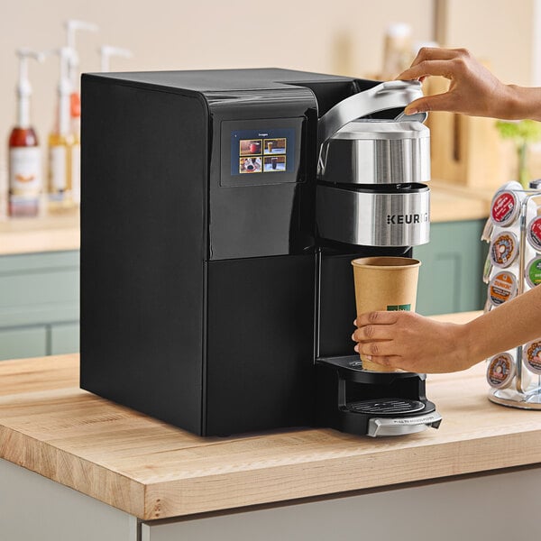 A person using a Keurig plumbed commercial single serve coffee maker to fill a cup of coffee.