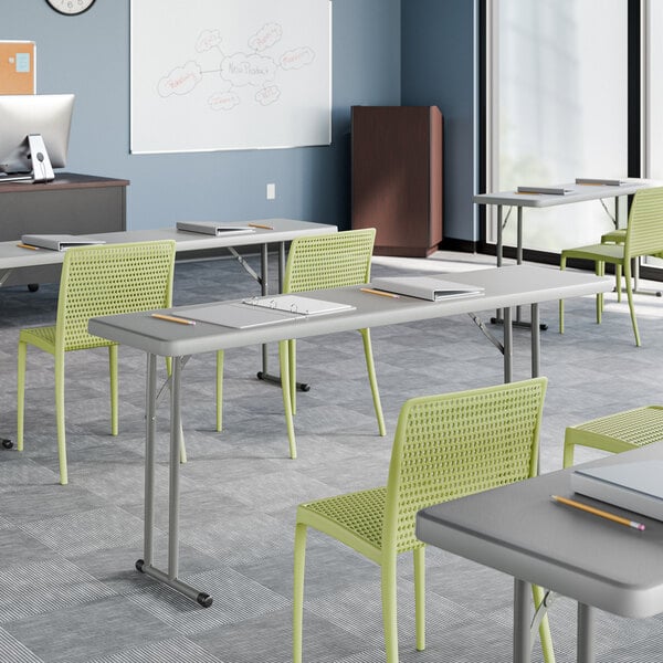 An 18-inch by 72-inch gray heavy-duty blow molded plastic folding table with gray legs, set up in a classroom setting.
