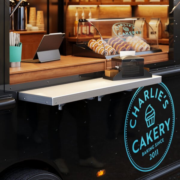 A Regency aluminum folding concession shelf mounted on a wall above a food truck counter.