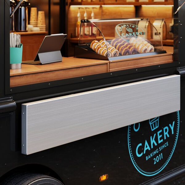 A Regency aluminum folding concession shelf on a counter in a food truck with pastries.