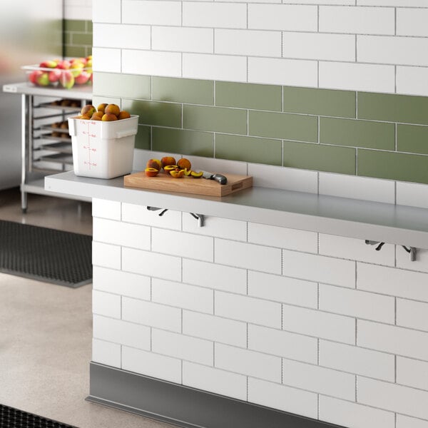 A Regency aluminum folding wall mount shelf over a counter with a bucket of fruit on it.