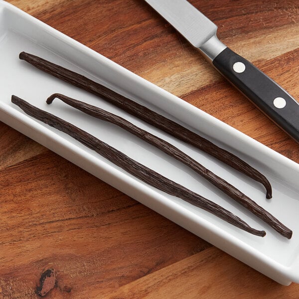 A white rectangular dish with several Hometown Provisions Gourmet Vanilla Bean tubes on it next to a knife.