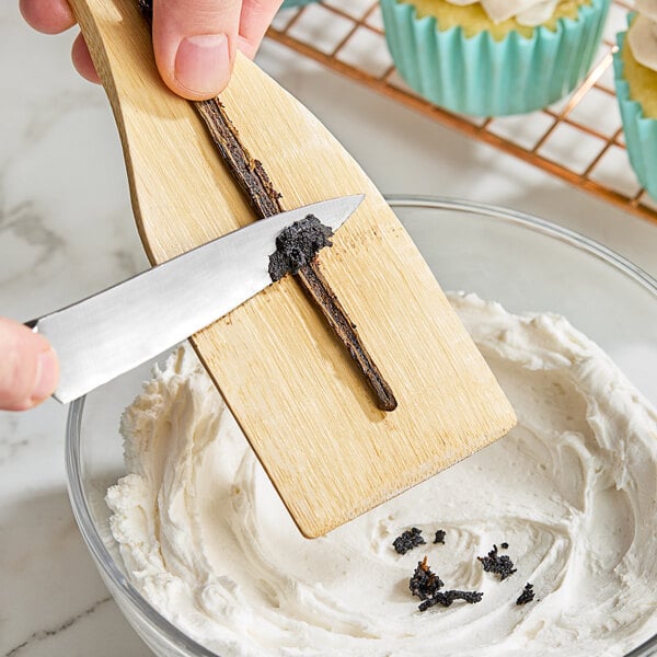 A person using a knife to cut open a Hometown Provisions Gourmet Vanilla Bean tube.