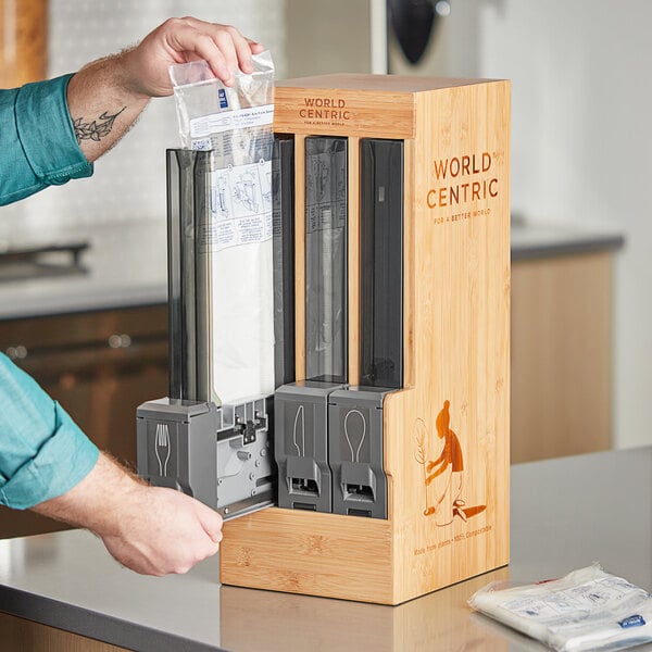 A person putting a bag of cutlery sleeves into a wooden box.