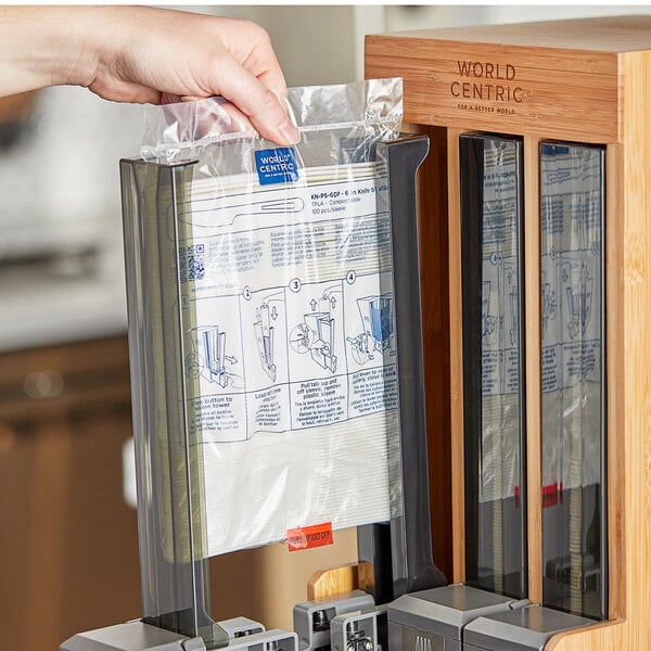 A hand using a World Centric TPLA knife refill sleeve in a professional kitchen to fill a paper dispenser.