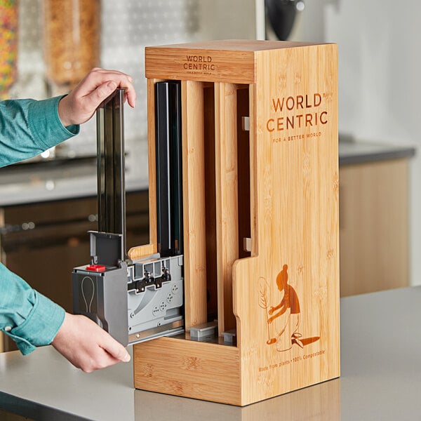 A person using a machine to put a World Centric Touchless Cutlery Dispenser into a box.